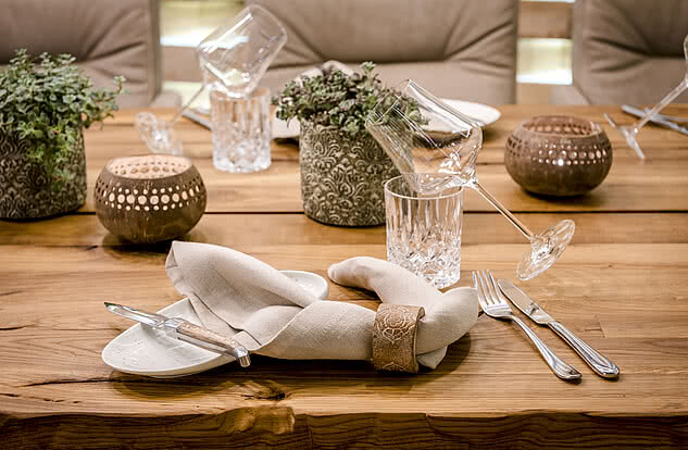 Detailreich gedeckter Holztisch im Genussdorf Gmachl mit stilvollen Servietten, Gläsern und dekorativen Kerzenhaltern.